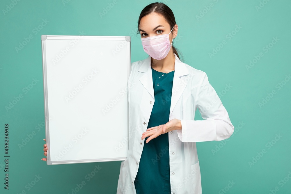 Woman doctor wearing a white medical coat and a mask holding blank board with copy space for text isolated on background. Coronavirus concept Woman doctor wearing a white medical coat and a mask holding blank board with copy space for text isolated on background. Coronavirus concept