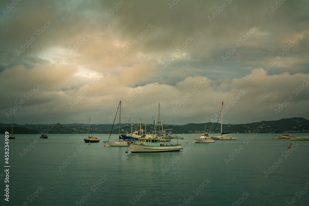 Evening clouds reflected in calm waters of a small harbour. Fishing and sailing boats anchored close to the shore