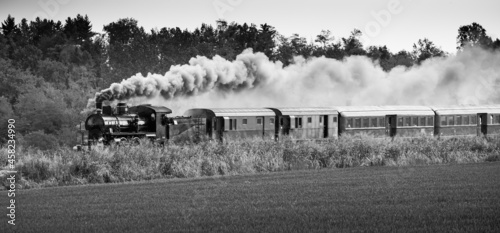 Steam train runs on the tracks in the countryside. Black and white photography.