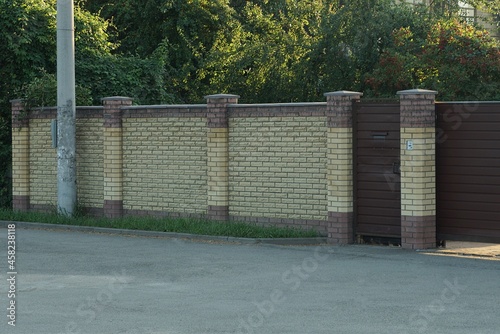 private long brown bricks fence wall with a closed iron door on the street