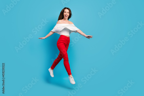 Photo of adorable impressed young woman dressed white blouse smiling jumping high empty space isolated blue color background