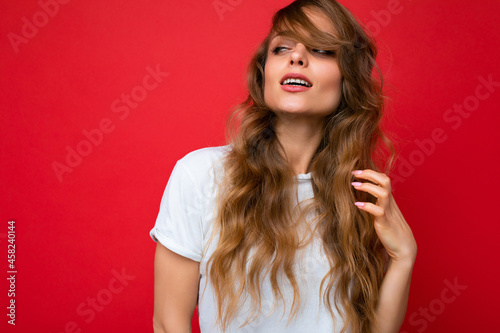 Young beautiful curly blonde woman with sexy expression, cheerful and happy face wearing casual white t-shirt isolated over red background with copy space