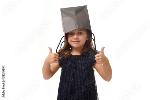 Portrait of beautiful Caucasian baby girl having fun, putting a black shopping packet on her head, looking at camera, showing thumbs up with her fingers. Black Friday concept