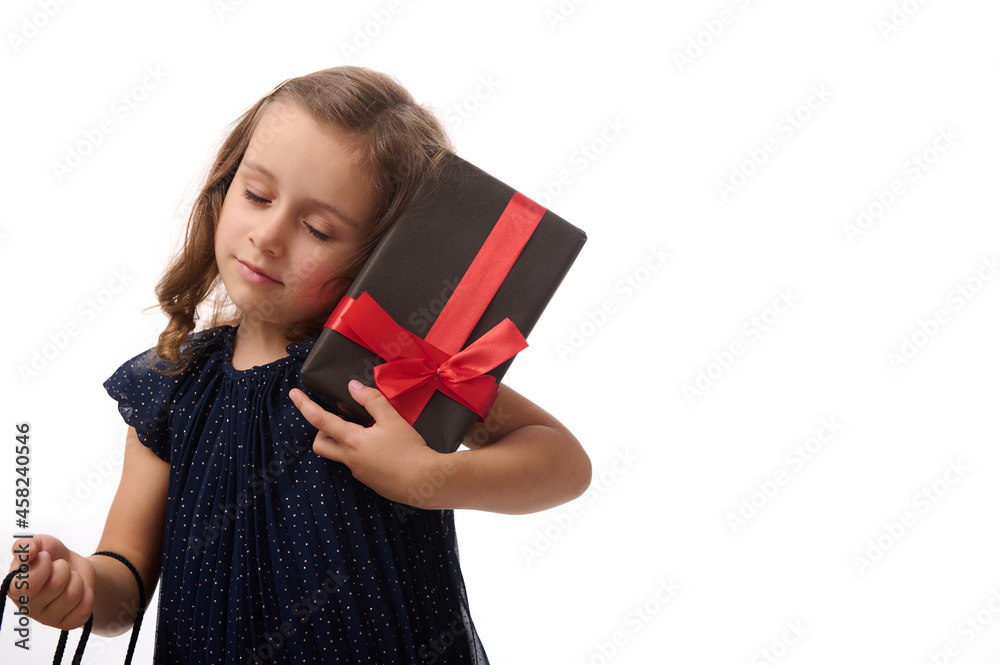 Portrait of a beautiful pretty 4 years old little girl with closed eyes holding a gift and shopping packet, posing against a white background with copy space. Black Friday concept Portrait of a beautiful pretty 4 years old little girl with closed eyes holding a gift and shopping packet, posing against a white background with copy space. Black Friday concept