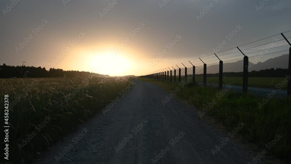 Magical sunset over countryside dirt road and airport fence. Summer evening. Farming field in the foreground. Handheld Magical sunset over countryside dirt road and airport fence. Summer evening. Farming field in the foreground. Handheld