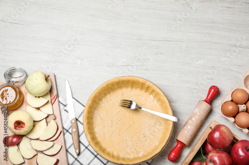 Flat lay composition with raw dough, fork and ingredients on white wooden table, space for text. Baking apple pie