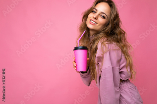 Photo of attractive young happy smiling brunette woman wearing everyday stylish clothes isolated over colourful background wall holding paper cup for cutout drinking tea looking at camera