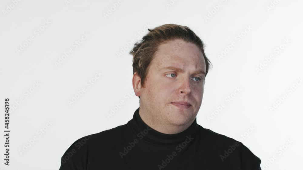 Medium close-up portrait of young man with poker face looking at camera indifferently standing at white background Medium close-up portrait of young man with poker face looking at camera indifferently standing at white background