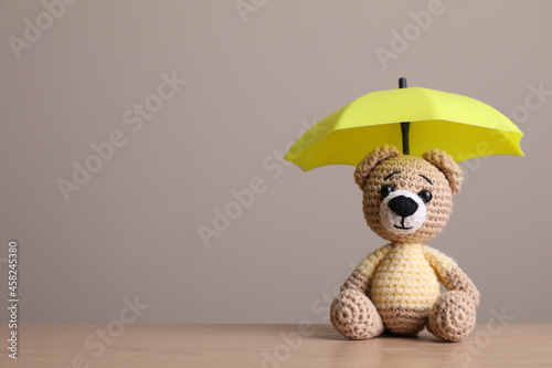 Small umbrella and toy bear on wooden table. Space for text