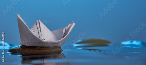 Paper origami boat on the stone in blue water. Photo with copy space.