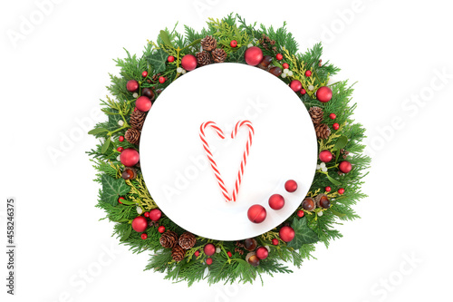Christmas table setting with plate, candy canes and red baubles with holly and winter greenery on white background. Fun composition for the holiday season. Top view, flat lay, copy space.