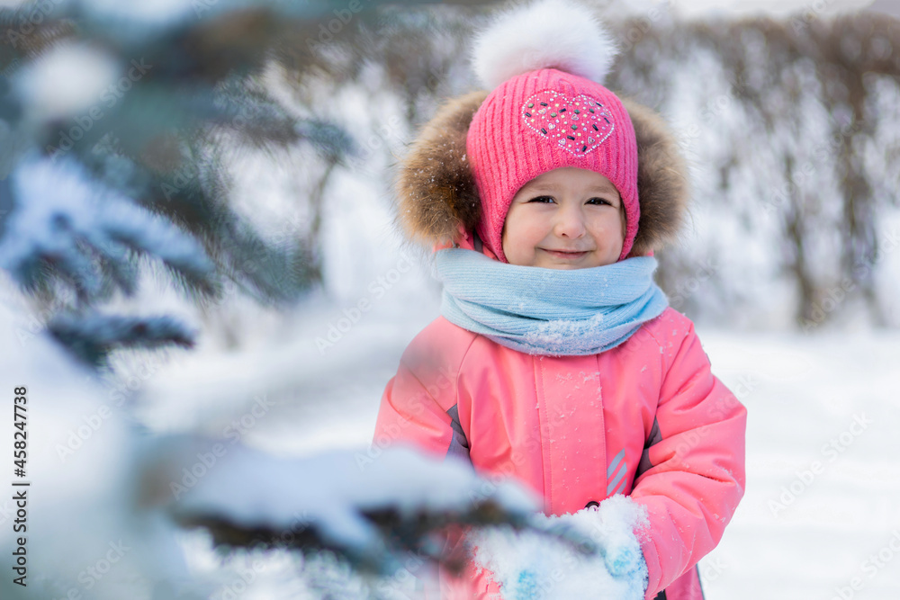 Funny little toddler girl in pink jumpsuit playing in snowballs. wintertime for children. winter games outdoors. Kid having fun at Christmas time