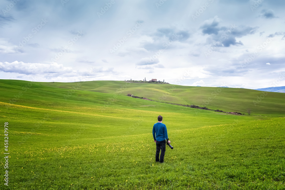 An alone photographer with camera in hands enjoys the amazing spring landscape in the heart of Tuscany in morning