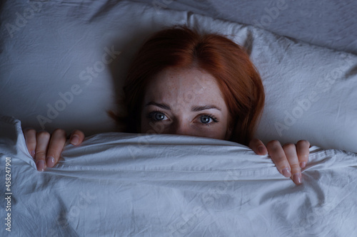 sleepless woman lying in bed hiding under duvet at night photo