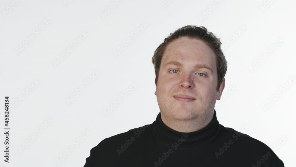 Medium close-up portrait with slowmo of young smiling man waving hand and looking at camera standing at white background in studio Medium close-up portrait with slowmo of young smiling man waving hand and looking at camera standing at white background in studio