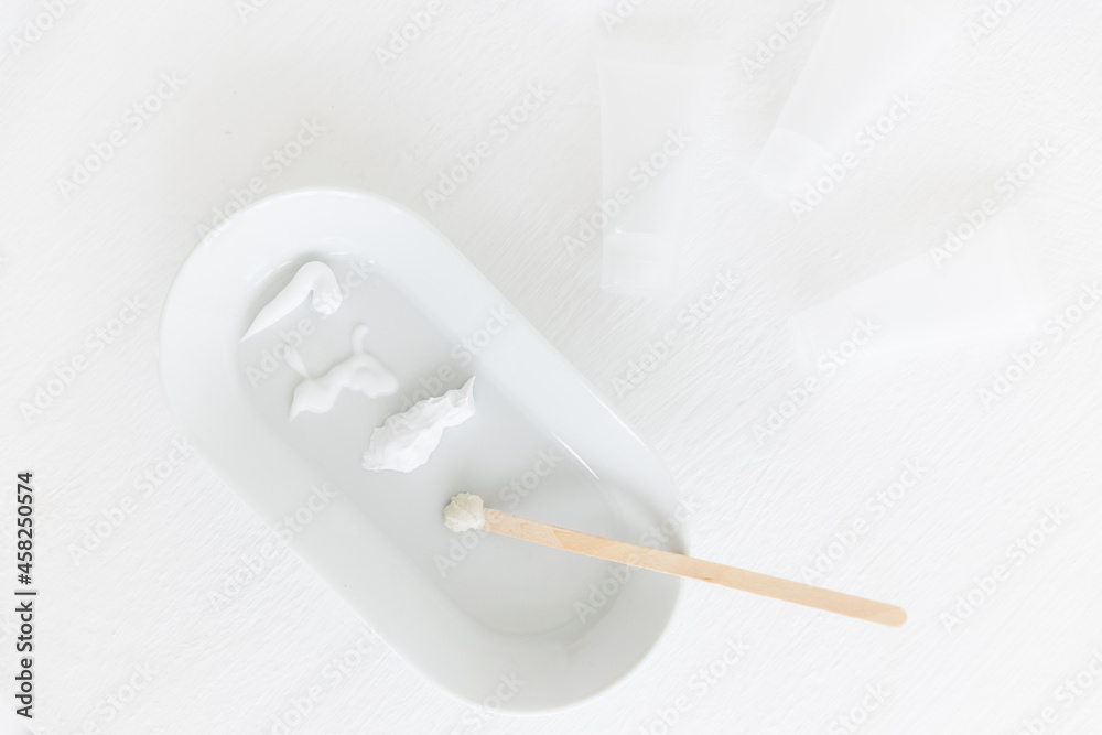 an oval saucer with smears of cosmetic cream. a wooden stick with cream is lying next to it. there are several creamy textures on a white background. Cosmetology and care. an oval saucer with smears of cosmetic cream. a wooden stick with cream is lying next to it. there are several creamy textures on a white background. Cosmetology and care.