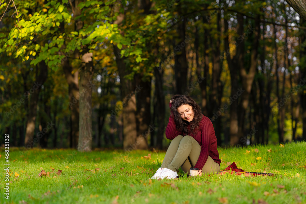 Pretty girl enjoys autumn and the beauty of nature sitting on a green lawn in the park. Autumn mood Pretty girl enjoys autumn and the beauty of nature sitting on a green lawn in the park. Autumn mood