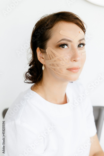 Portrait of a young Caucasian girl in a white coat with tapes on her face. she covers her face with duct tape. A young woman with ribbons on her face. An aesthetic patch for the face. a patch to maint