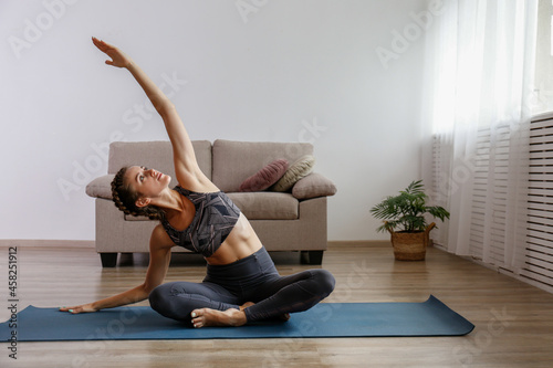 Sporty young woman practicing yoga in the comfort of her own home. Yogini performing morning physical exercise routine at the living room. Interior background, copy space, close up.