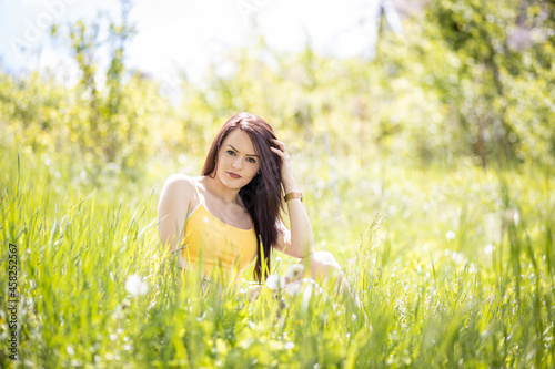 Young woman in yellow top sitting in grass in summer