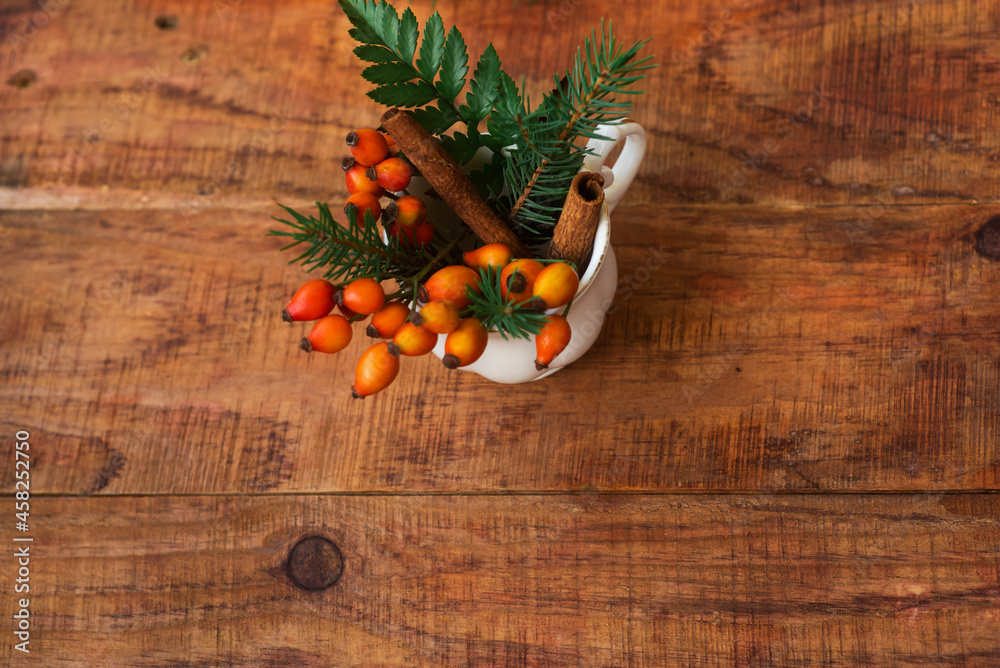 Winter, warm atmosphere. A composition with a cup with spruce branches and rosehips on a wooden background Winter, warm atmosphere. A composition with a cup with spruce branches and rosehips on a wooden background