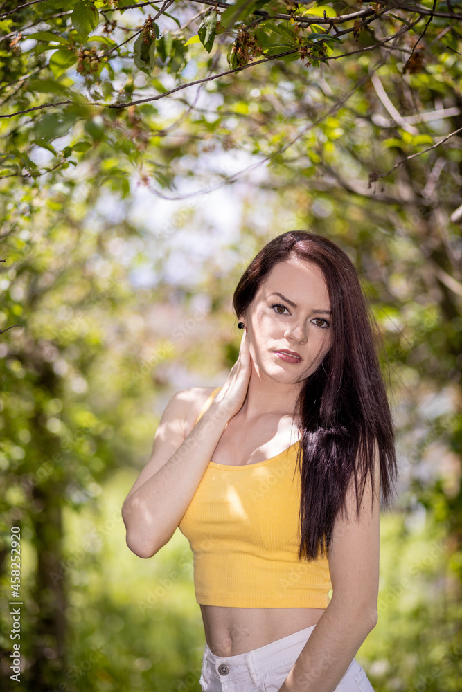 Young woman in yellow top and white shorts standing under trees in summer Young woman in yellow top and white shorts standing under trees in summer