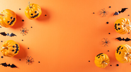Halloween decorations made from pumpkin, paper bats and black spider on orange background. Flat lay, top view with copy space for text.