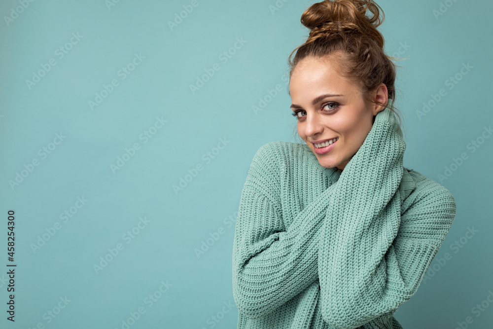 Obraz premium Young beautiful cute curly blonde woman with sexy expression, cheerful and happy face wearing trendy blue sweater isolated over blue background with copy space