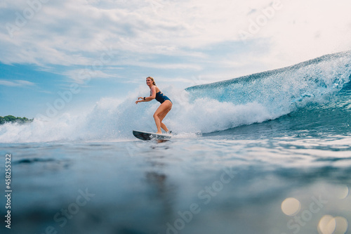 Surfer girl at surfboard on wave in tropical ocean. Sporty woman during surfing.