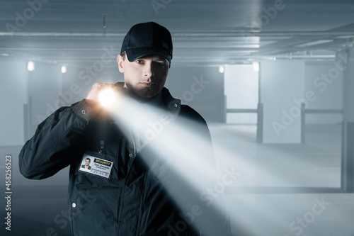 Security guard with flashlight at door in empty parking garage