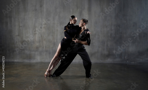 The young millennial dance ballroom couple in black dress dancing in sensual pose on studio background. Professional dancers dancing latino. Hobby dance concept. Human emotions - love and passion