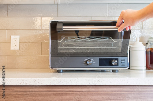 Hand pulling down a digital countertop oven door photo