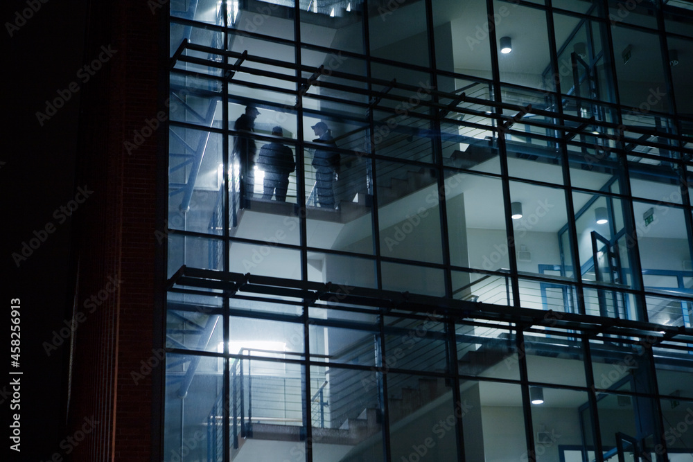 Silhouettes of security guards seen through office building windows at night