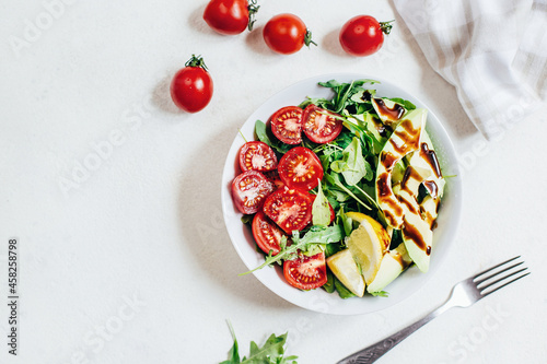 top view of tomato salad arugula avocado lemon in white plate on light background