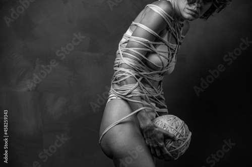 Beautiful woman wrapped in a rope over grey wall 