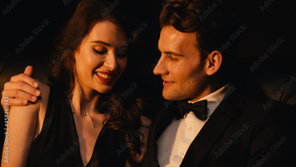 cheerful man looking at pretty woman smiling isolated on black