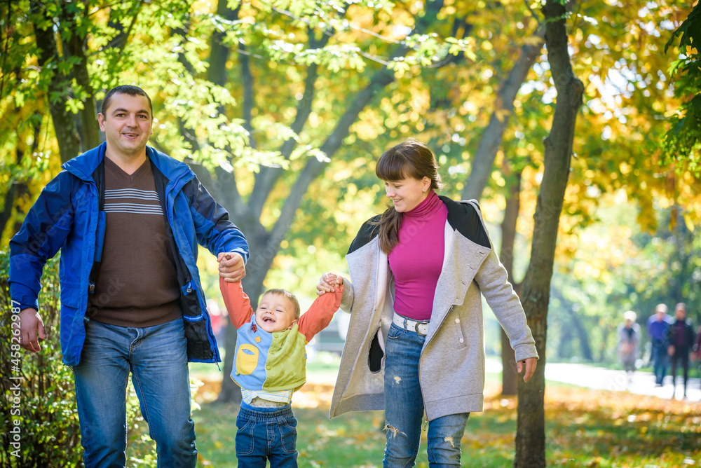 Beautiful young family on a walk in autumn forest on maple yellow trees background. Father and mother hold son on hands. Happy family leisure together concept Beautiful young family on a walk in autumn forest on maple yellow trees background. Father and mother hold son on hands. Happy family leisure together concept