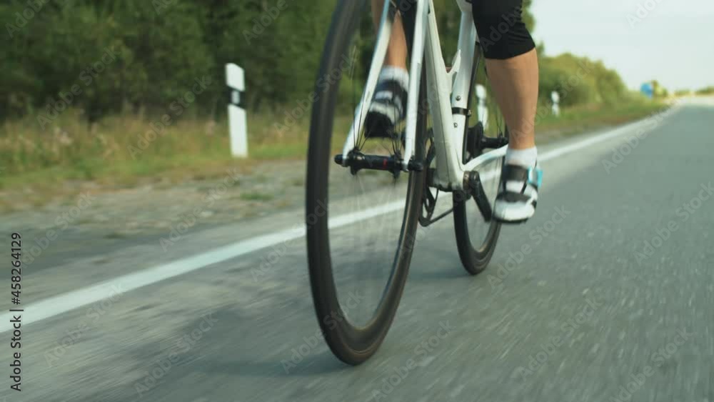 Tilt up shot of female triathlete in helmet and sunglasses riding sport bike on road while training for triathlon competition