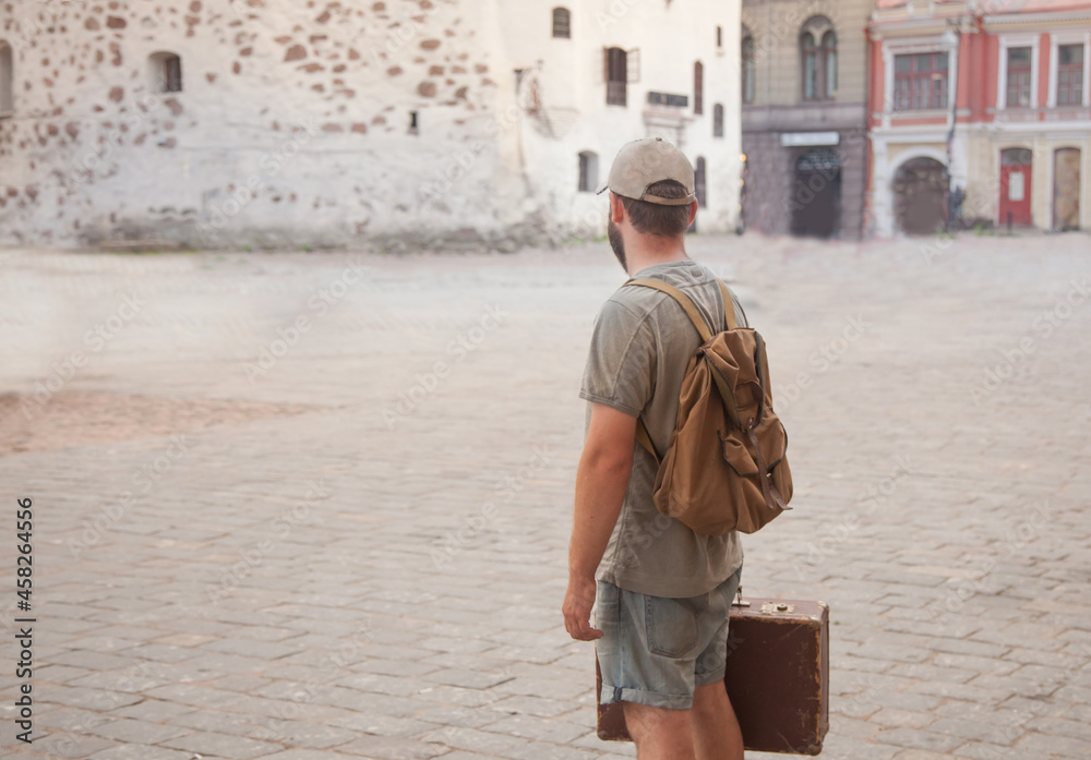 a man with a beard is standing in an ancient city with a vintage backpack and a suitcase. the concept of travel. copy space