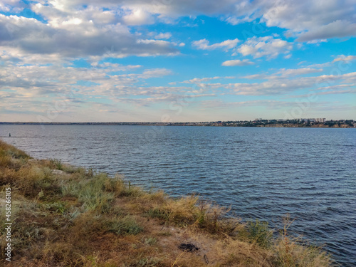 large river with blue water with waves and white clouds above the cliff