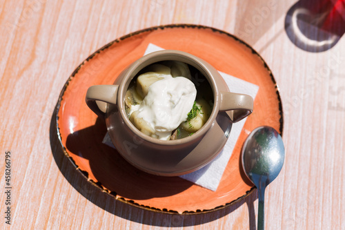 A deep plate with Siberian dumplings and sour cream on table in an outdoor cafe.