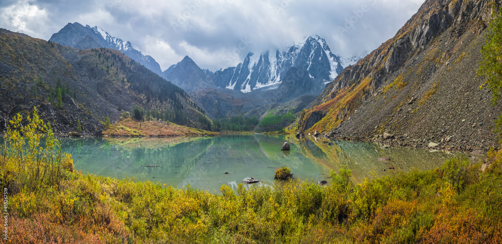 Fototapeta premium Autumn sunny alpine landscape with beautiful shallow mountain lake with streams in highland valley from bigger mountains under cloudy sky. Upper Shavlin Lake in the Altai.