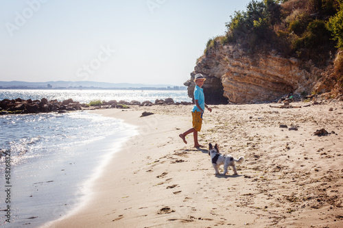 Beautiful young boy and dog walking together on the beach
