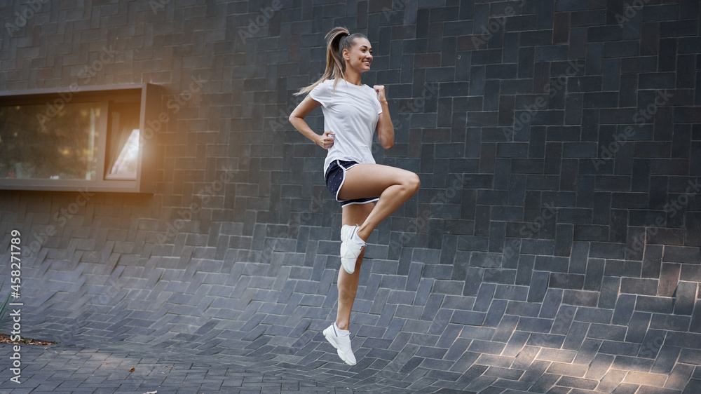 Fototapeta premium Woman with fit body jumping and running against black wall background