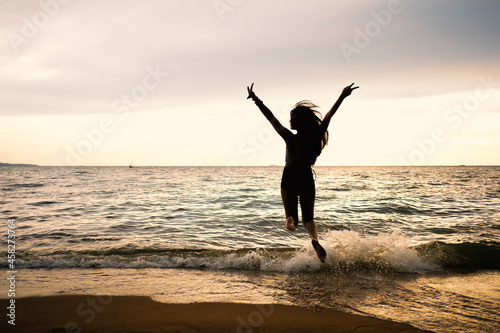 Silhouettes of people on the beach, lady jumping at sand beach. Relaxing, fun, and enjoy holiday at tropical paradise beach with blue sky and white clouds. Girl in summer vacation.