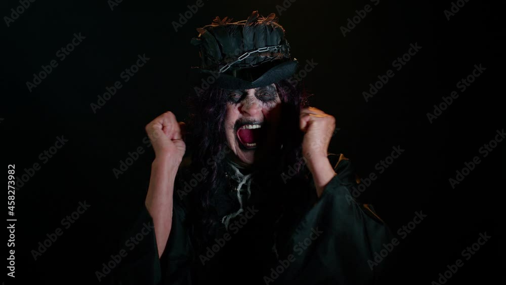 Frustrated sinister woman with horrible scary Halloween witch makeup raising hands in indignant expression, quarreling, asking reason of conflict, why such stubborn. Vampire granny on black background