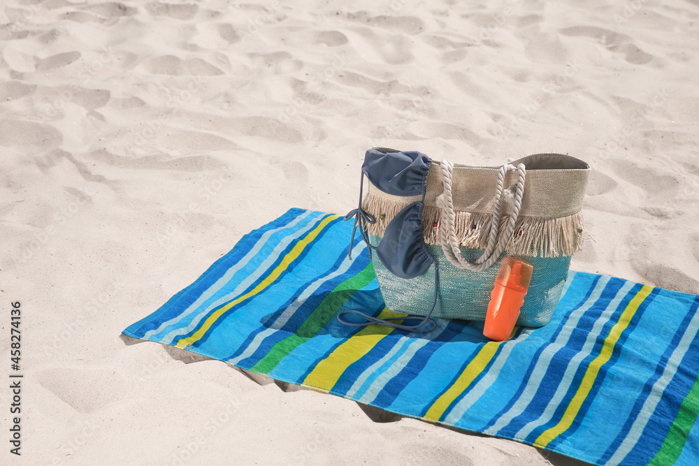 Striped beach towel and bag with accessories on sand