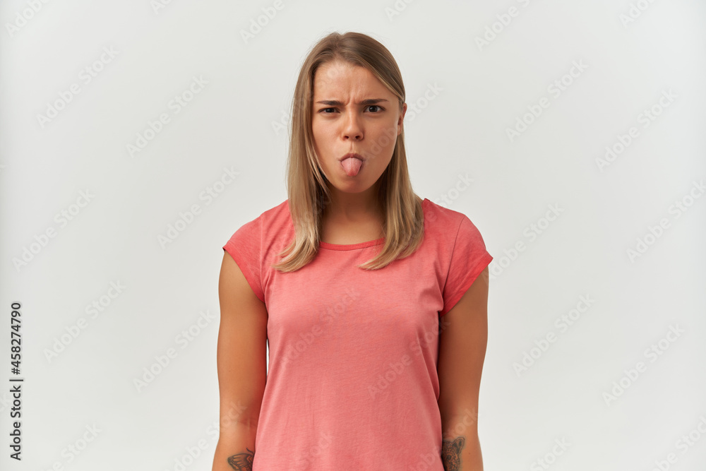 Young adult female, shows her tongue with negative, upset facial expression. Isolated over white background Young adult female, shows her tongue with negative, upset facial expression. Isolated over white background
