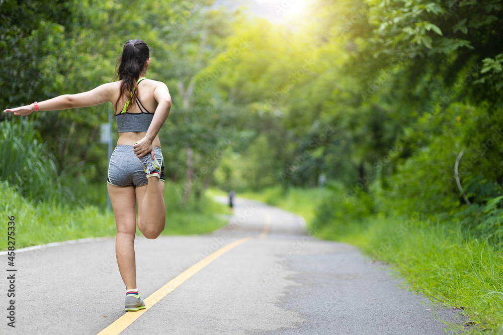 A female runner warms up and stretches before jogging in the park. A female runner warms up and stretches before jogging in the park.