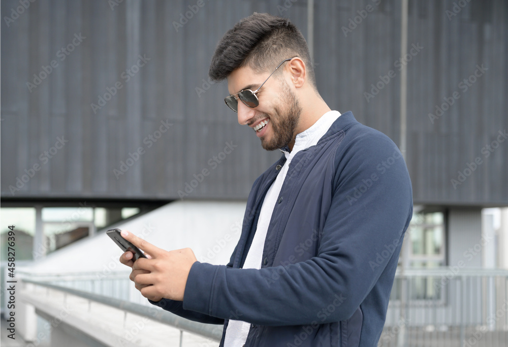 Handsome man using mobile phone app texting outside of office in urban city with skyscrapers buildings in the background. Young man holding smartphone for business work. High quality photo Handsome man using mobile phone app texting outside of office in urban city with skyscrapers buildings in the background. Young man holding smartphone for business work. High quality photo